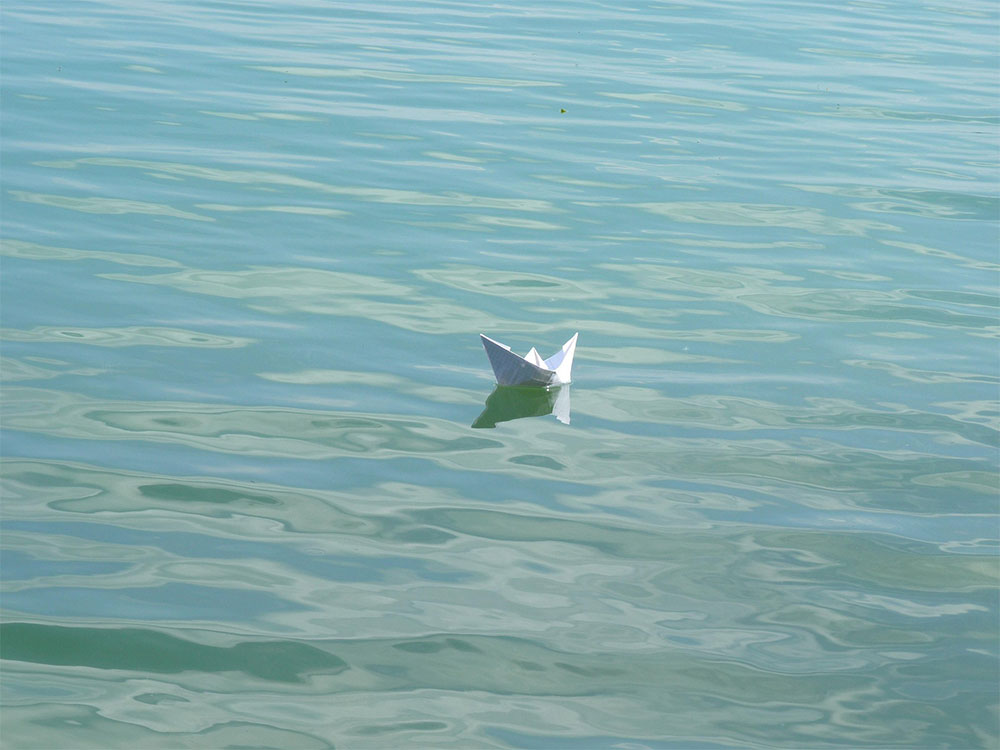 Paper boat bobbing on water to make the point that most people go through life where the current takes them, without a plan.
